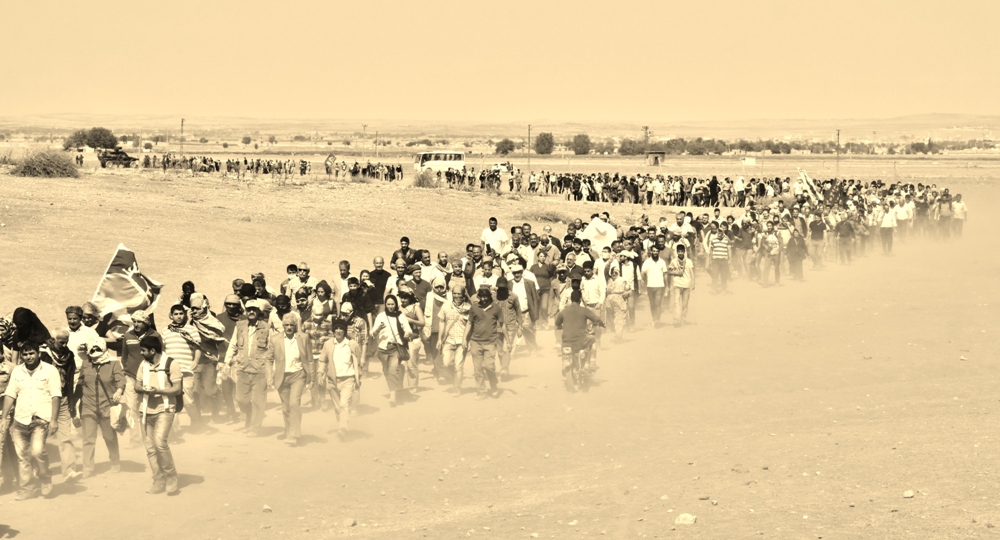 Kitle sınırı aşıp mayınlı araziden Kobanê'ye yürüyor. Kobanê halkı mayınlı arazide yol güvenliğimizi sağlıyor.