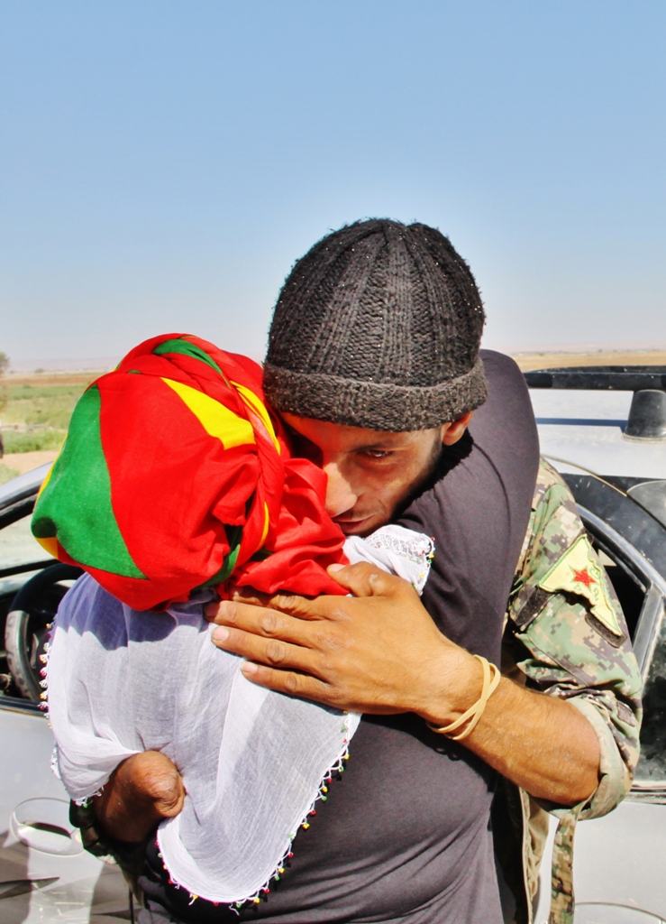 Tek eliyle Daiş çetelerine karşı savaşan YPG savaşçısını göğsüne basan bir ana. Evladını koklar gibi kokluyor savaşçıyı. 